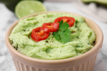 Bowl of delicious guacamole with chili pepper on white table, closeup