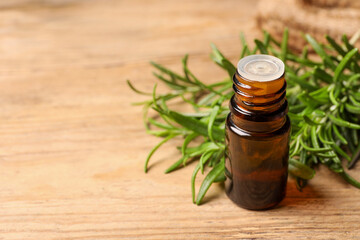 Bottle with essential oil and fresh rosemary on wooden table, space for text