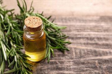Bottle of essential oil and fresh rosemary on wooden table, closeup. Space for text