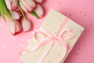 Fototapeta na wymiar Beautiful gift box with bow, tulips and confetti on pink background, flat lay