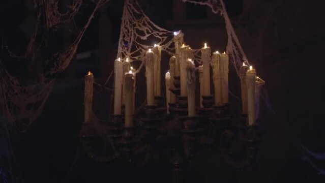 This video shows an old, antique candelabra covered with cobwebs and flickering to illuminate a dark rom.