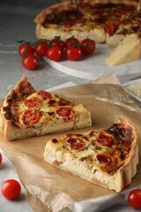 Pieces of delicious homemade quiche with prosciutto and tomatoes on light grey marble table