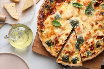 Delicious homemade quiche and ingredients on white table, flat lay