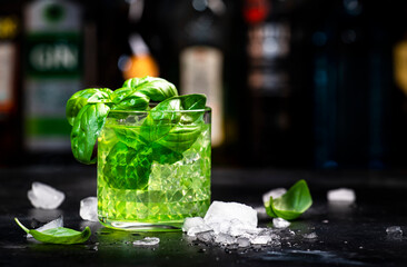 Basil smash alcoholic cocktail drink with dry gin, syrup, lemon, basil and ice, dark bar counter...