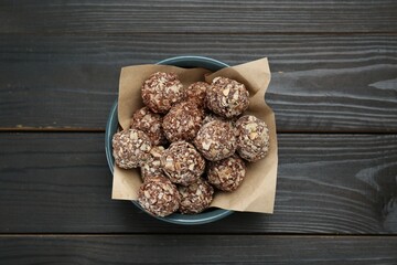 Bowl of delicious sweet chocolate candies on dark wooden table, top view