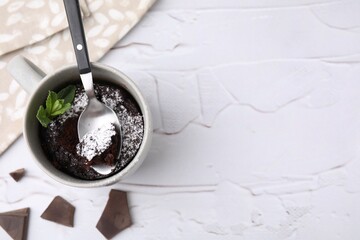 Tasty chocolate mug pie, mint and spoon on white textured table, flat lay with space for text. Microwave cake recipe