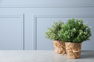 Different artificial potted herbs on light grey table near wall, space for text