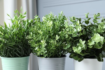 Different artificial potted herbs near light grey wall, closeup