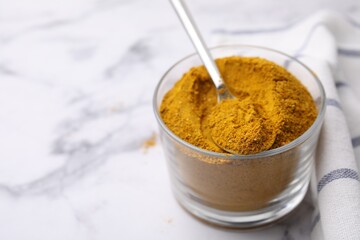Glass with curry powder and spoon on white marble table, closeup. Space for text