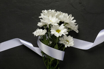 Beautiful chrysanthemum flowers and white ribbon on black table, top view. Funeral symbols - obrazy, fototapety, plakaty