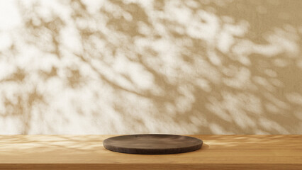 Round wooden plate on the wooden table with light wall background. Leaves shadow on the wall.