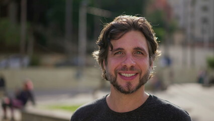 Young man close-up face standing in city park smiling at camera. A handsome male caucasian person in 30s portrait