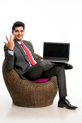 Young indian businessman sitting on chair and showing laptop screen.