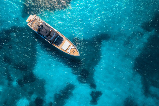 Aerial view of luxury yacht on blue sea at sunset in summer. Travel and yachting in Sardinia, Italy. Drone view from above of speed boat, sea lagoon, transparent azure water. Seascape. Vacation