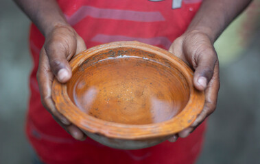 A boy holds a terracotta pot with his both hand and the background blur