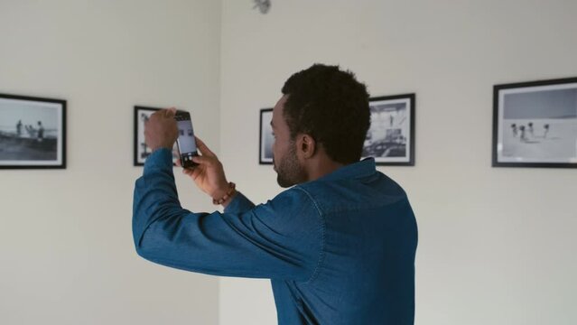 Young black man taking pictures with smartphone of photo exhibition in modern art gallery