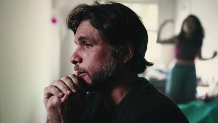 Stressed boyfriend listening to screaming girlfriend arguing with him in background. couple fighting in bedroom. Male person sitting by bedside suffering from a bad relationship