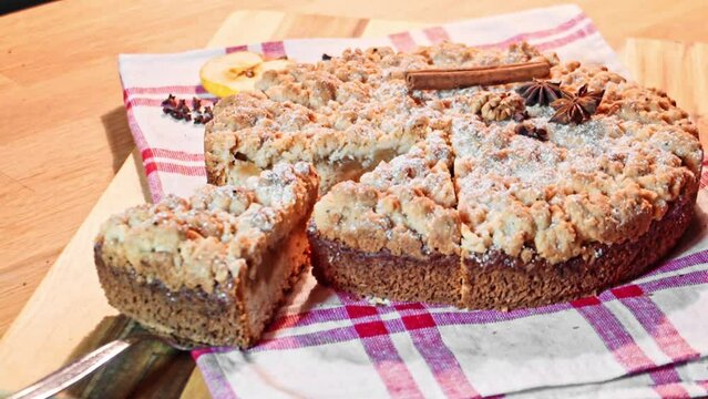 Apfelkuchen mit Streuseln angerichtet auf einem Holzbrett mit einer kleinen wei&szlig;en Tischdecke mit rotem Muster
