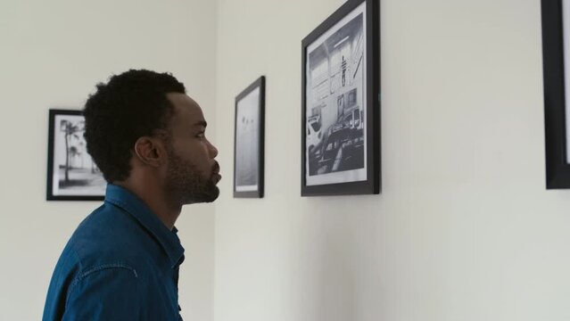 Young African American man taking pictures with smartphone of photo exhibition in art gallery