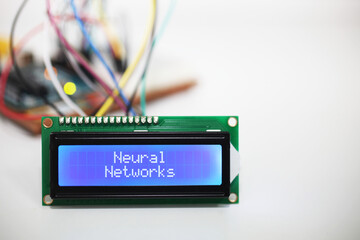 Blue LCD Display displaying the words 'Neural Networks' with a microcontroller and connecting wires...