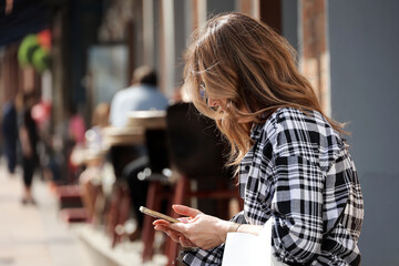 Young woman sitting with smartphone in hands on city street