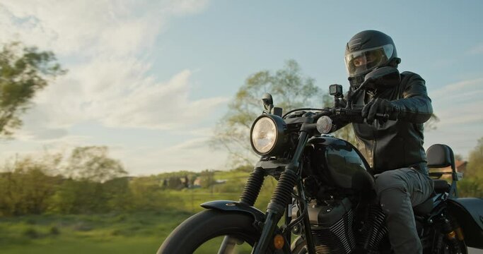 Low-angle tracking shot of a man driving a motorcycle through a country road. 