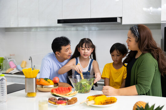 Happy Asian Family Working  Together To Prepare Dinner In  Kitchen At Home.