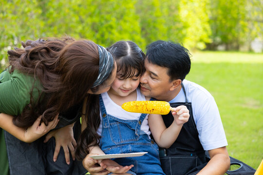 Mother making Toasted corn. Asian family in backyard garden at home. Home camping and cooking Barbeque party. Happy Asian family enjoying BBQ camping at home