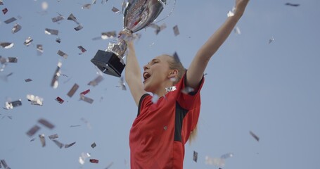 Portrait of Caucasian female soccer football player celebrating victory in the championship, lifting the trophy above her head in a huge stadium