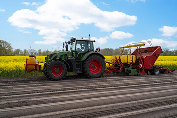 Fototapeta premium Seitliche Ansicht einer modernen roten Kartoffellegemaschine mit grünen Traktor, beim Kartoffel legen im Frühjahr.