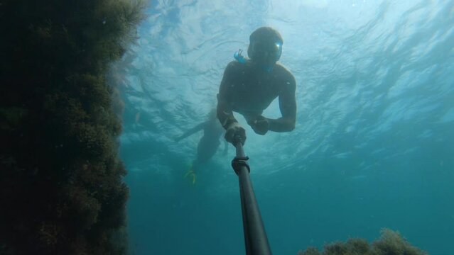 Shot of a man underwater wearing a mask, swimming underwater and taking a selfie during the day on the seabed, floating in the air of a sunken ship covered in algae