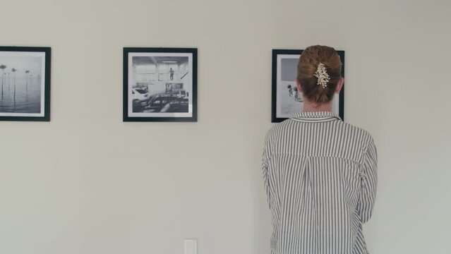 Young female visitor walking in gallery and looking at black and white photos on walls on art exhibition