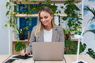 Smiling young businesswoman using laptop and digital tablet at desk