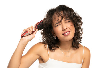 Fototapeta premium Young dark skinned woman with makeup has a problem with combing her wavy hair on a white background