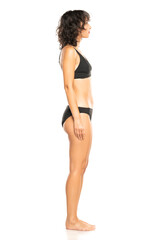 Young exotic brunette woman in black bikini swimsuit posing on a white background. Profile, sidet...