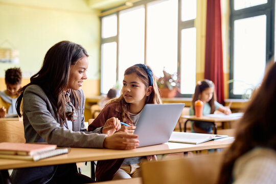 Happy teacher and schoolgirl using laptop during computer class in classroom.