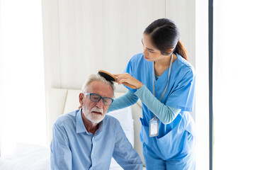 comb hair for old people. Asian female caregiver helping senior caucasian male dress up at home...