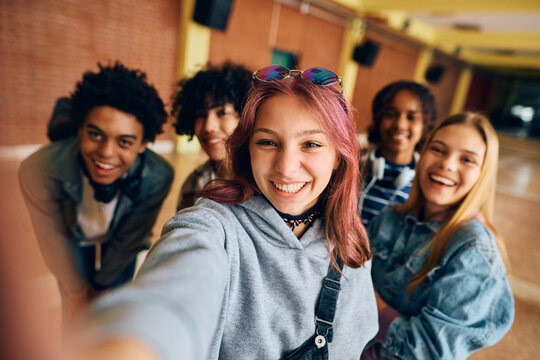 Cheerful teenagers have fun while taking selfie in high school hallway.