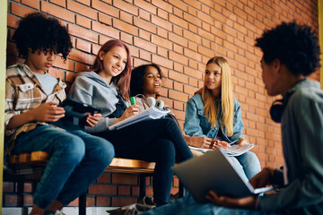 Multiracial group of high school friends talk while studying in hallway.