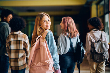 Happy high school student looking at camera while going on class with her friends.