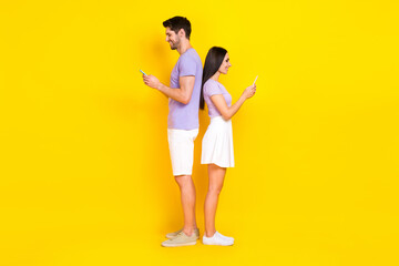 Full body photo of pretty young girl male hold telephone back to back texting wear trendy purple outfit isolated on yellow color background