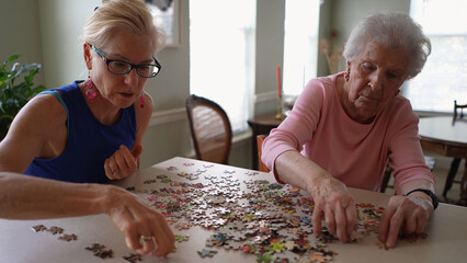 Happy mature woman doing puzzle and spending time with elderly senior old woman at home.