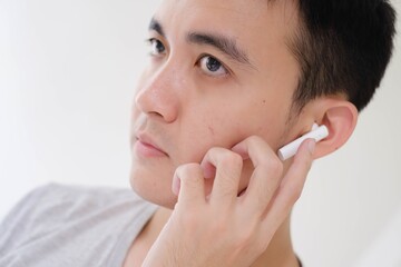 Close-up shot of the partial face of a young Asian man listening to white true wireless stereo...