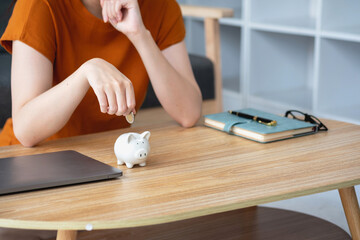 Young Asian woman saving for retirement Saving money through a piggy bank and taking notes on notebook, savings concept.