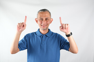 Fototapeta premium Asian man wearing tshirt pointing fingers up at copy space isolated over white background. 