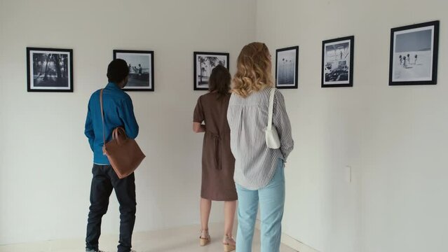 Full shot of people watching photo exhibition in art gallery, one woman taking pictures with smartphone