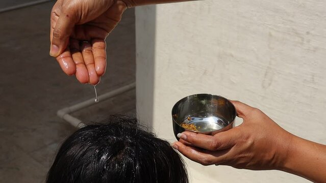 Applying coconut oil mixed with fenugreek seeds and curry leaves to head of a kid to nourish the hair, health care concept