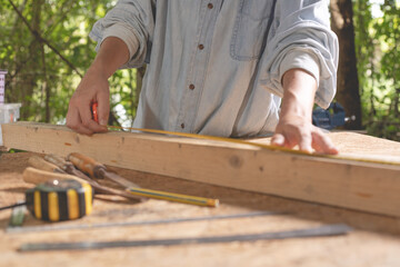 Female use tape measure to assemble wooden pieces. Professional carpenter at work measuring wooden...