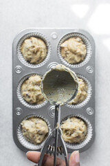 scooping chocolate chip muffin batter into a cupcake tin, An ice cream scoop being used to portion muffin batter into a cupcake pan, process of making muffins