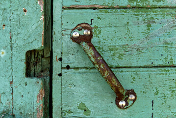 A close up of a rusty handle on old green wooden door